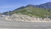 A scenic coastal road in Muğla with a sleek transfer vehicle driving along.