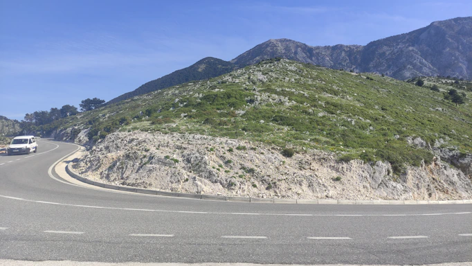 A scenic mountain road winding through lush green hills near Badrinath, with a taxi driving along.