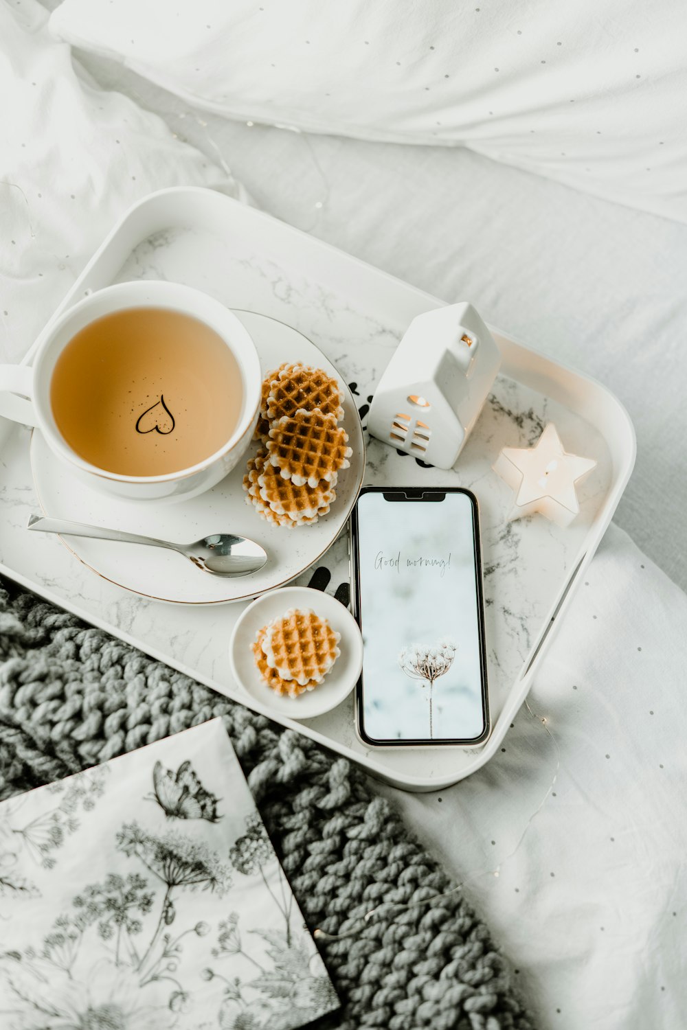 a tray with a cup of tea, waffles, and a cell phone