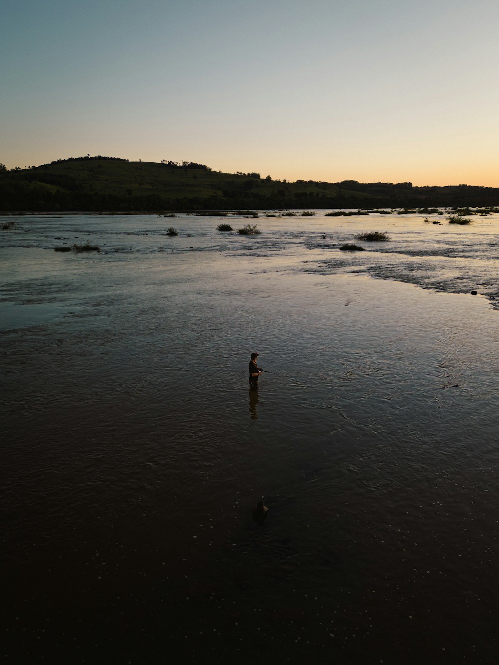 a person wading in shallow water at sunset