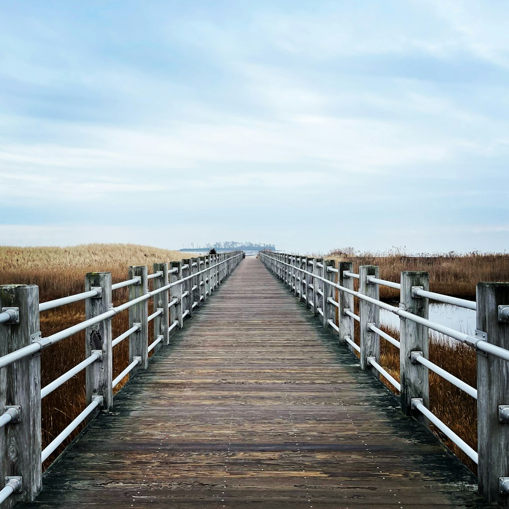 a wooden bridge with a white fence and a field in the background