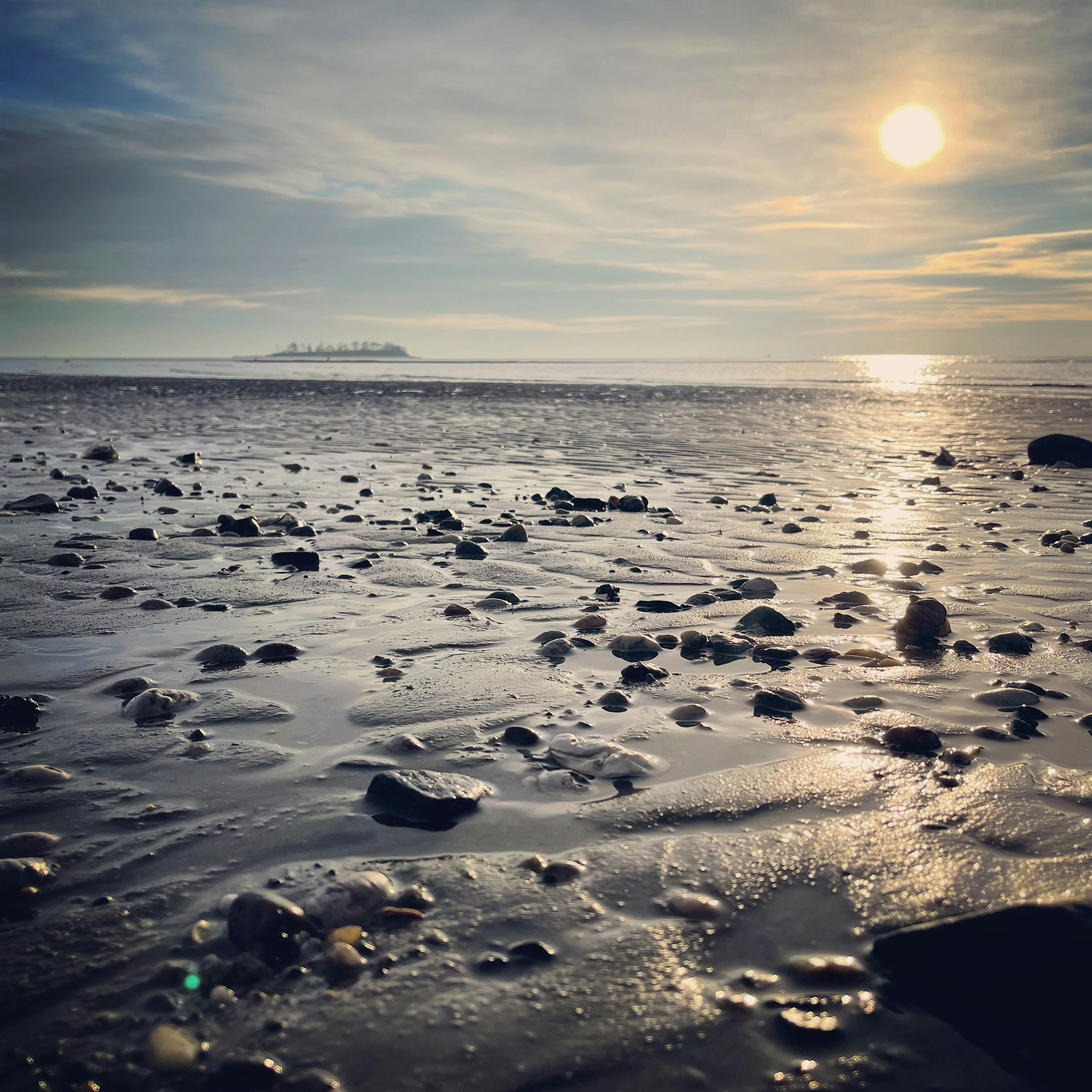 the sun is setting over the ocean with rocks in the water
