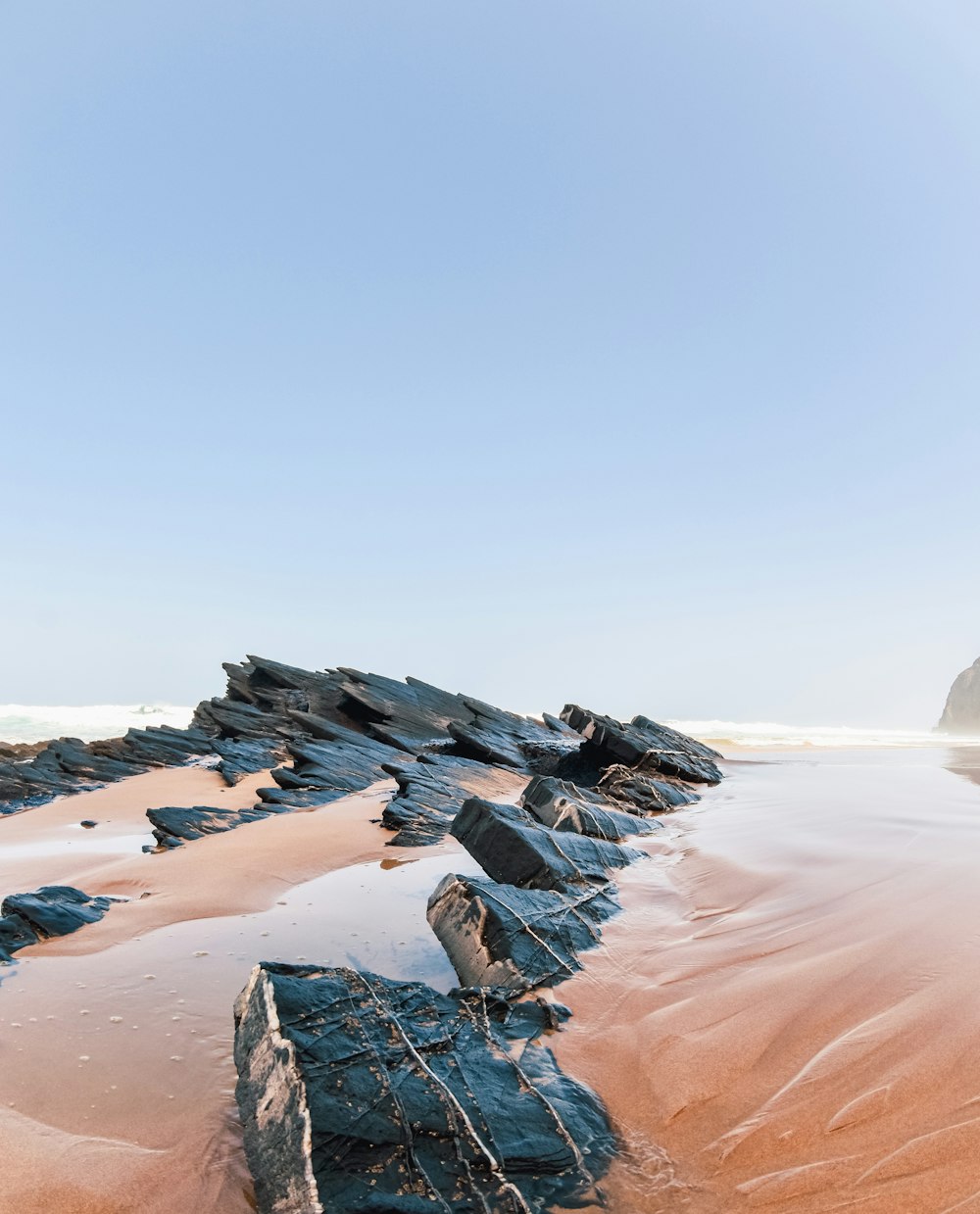 a beach with rocks and sand under a blue sky