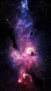 Vivid hues of purples, blues, and pinks blend seamlessly with specks of white representing distant stars against a backdrop of deep space. A celestial cloud of gas and dust forms a nebula, illuminated by the light of nearby stars. Amidst the vibrant colors, a small, dark planet orbits in the foreground.