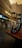 A motorcycle helmet rests on a brown wooden bench in an indoor shopping area with various storefronts displaying signs and menus. The background is blurred, highlighting the helmet in the foreground.