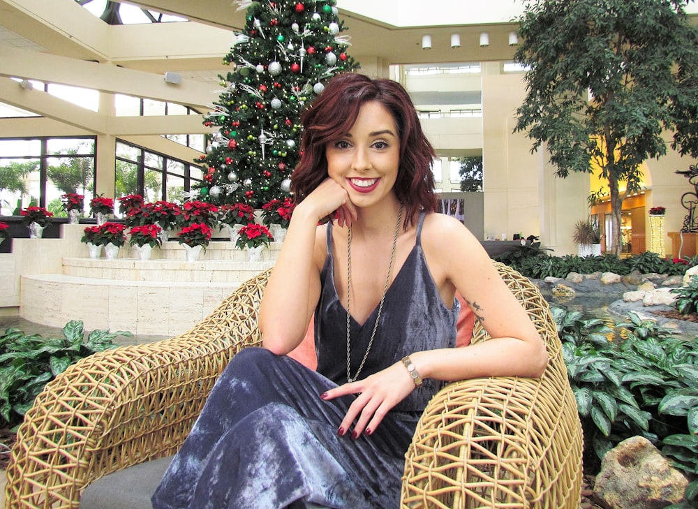 a woman sitting on a wicker chair with a christmas tree in the background
