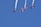 Four aerobatic airplanes fly closely together in an inverted formation, leaving white smoke trails against a clear blue sky. The planes display vibrant colors and branding on their wings.