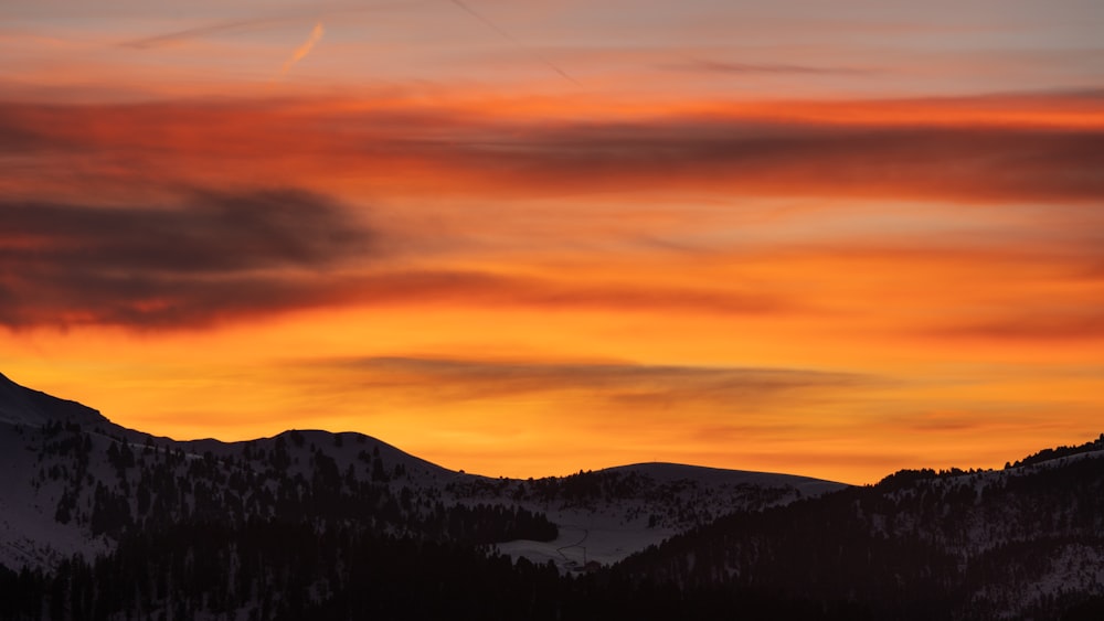 a sunset view of a mountain range with a plane flying in the sky