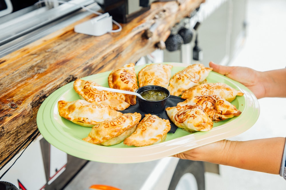 a person holding a plate of food with dipping sauce