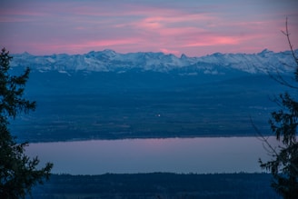 Sunset behind snow-capped mountains with a colorful sky reflecting on a calm lake.