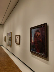 Display of various framed artworks hanging on a warm-toned gallery wall.