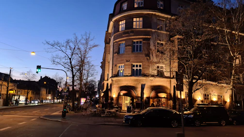 A vibrant street corner at dusk with warm orange and red lights glowing against a deep blue night sky.