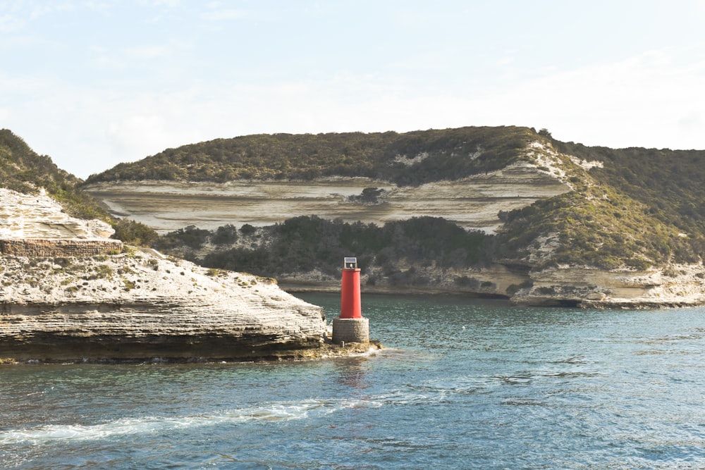 a red light house in the middle of a body of water