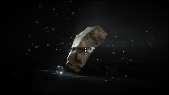 A large, rugged stone levitates in a dark environment, encircled by a metallic band. Small light particles float around, and a luminous sphere rests on the ground beneath the stone, casting a soft glow.