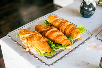 A beautifully arranged tray of croissant sandwiches with fresh greens and colorful fillings.
