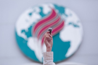 A hand is raised, holding a small gavel against a backdrop featuring an abstract representation of a globe with blue continents and a stylized red and teal flame design across it. The focus is on the hand and gavel, with the background slightly blurred.