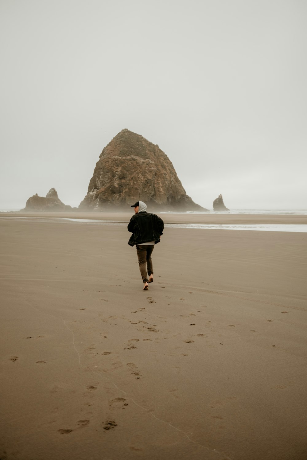 a person walking on a beach with a rock in the background