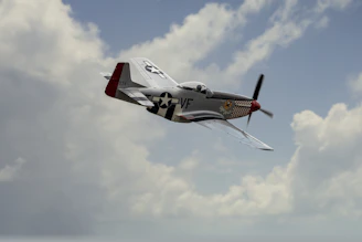 A vintage World War II fighter plane soaring above a cloudy battlefield at dawn.