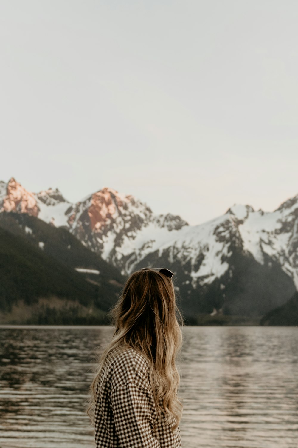 uma mulher em pé na frente de um lago com montanhas no fundo
