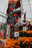 A scene full of vibrant marigold flowers showcasing artistic skeleton figures adorned with colorful clothing and intricate designs. The figures are stylized with bold patterns and bright accents, embodying the festive and cultural elements associated with the Day of the Dead celebration.