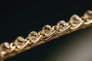 Close-up of a bracelet featuring a series of faceted, translucent stones or crystals, set in an intricately woven gold chain. The image focuses on the sparkle and clarity of the stones, giving a sense of luxury and elegance.