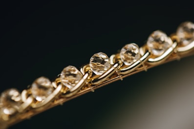 Close-up of a bracelet featuring a series of faceted, translucent stones or crystals, set in an intricately woven gold chain. The image focuses on the sparkle and clarity of the stones, giving a sense of luxury and elegance.