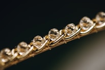 Close-up of a bracelet featuring a series of faceted, translucent stones or crystals, set in an intricately woven gold chain. The image focuses on the sparkle and clarity of the stones, giving a sense of luxury and elegance.