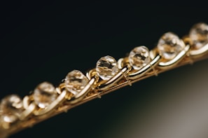 Close-up of a bracelet featuring a series of faceted, translucent stones or crystals, set in an intricately woven gold chain. The image focuses on the sparkle and clarity of the stones, giving a sense of luxury and elegance.
