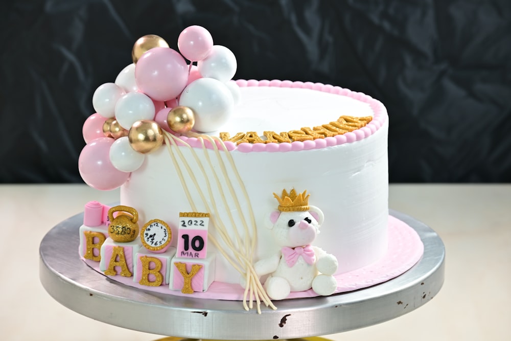 a pink and white cake with balloons and a teddy bear