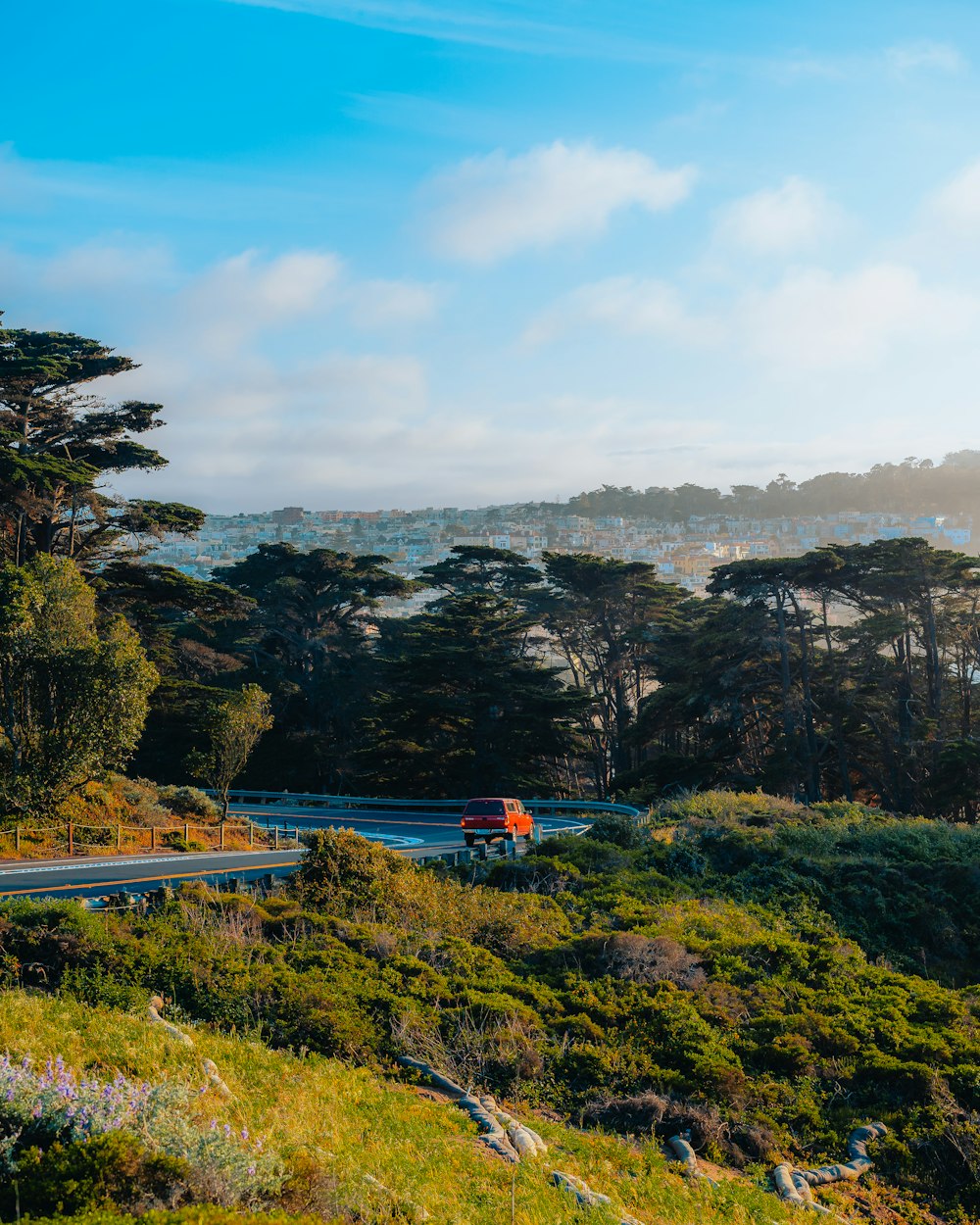 a truck driving down a road next to a lush green hillside