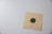 A paper card featuring a black and white concentric circle bullseye target with a single hole in it. There is a number 010408 printed below the target, and the card is laid on a light gray surface.