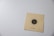 A paper card featuring a black and white concentric circle bullseye target with a single hole in it. There is a number 010408 printed below the target, and the card is laid on a light gray surface.