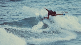 A surfer expertly maneuvers through a breaking wave, displaying skill and balance on a surfboard. The water is a vibrant blue, with white foamy crests surrounding the surfer, capturing the dynamic nature of the ocean and the thrill of surfing.