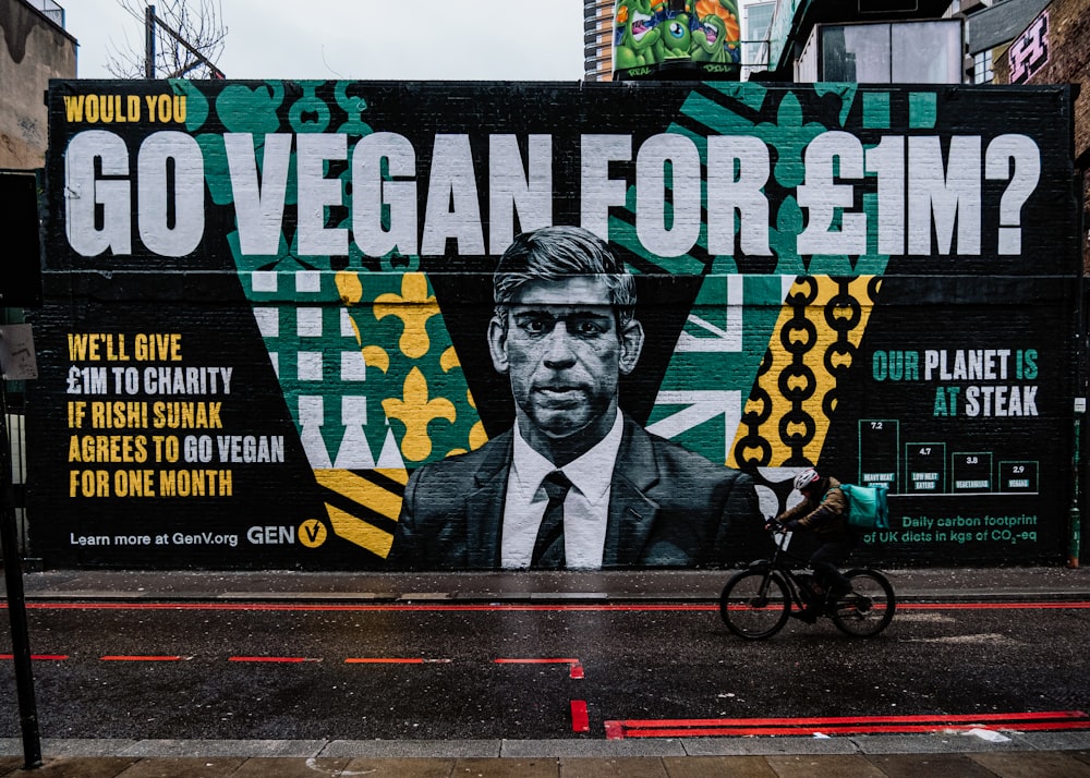 a man riding a bike past a large mural of a man in a suit