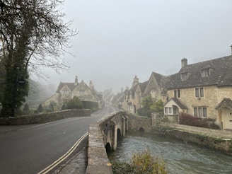 A foggy village street lined with old stone cottages, faint silhouettes of two figures meeting under a sprawling oak tree.