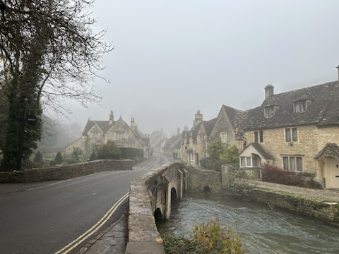 A foggy village street lined with old stone cottages, faint silhouettes of two figures meeting under a sprawling oak tree.