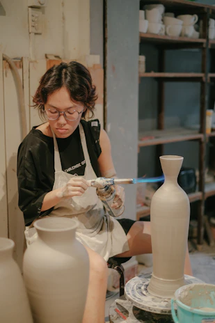 An artisan carefully glazing a freshly thrown clay vase in a cozy studio filled with pottery tools.