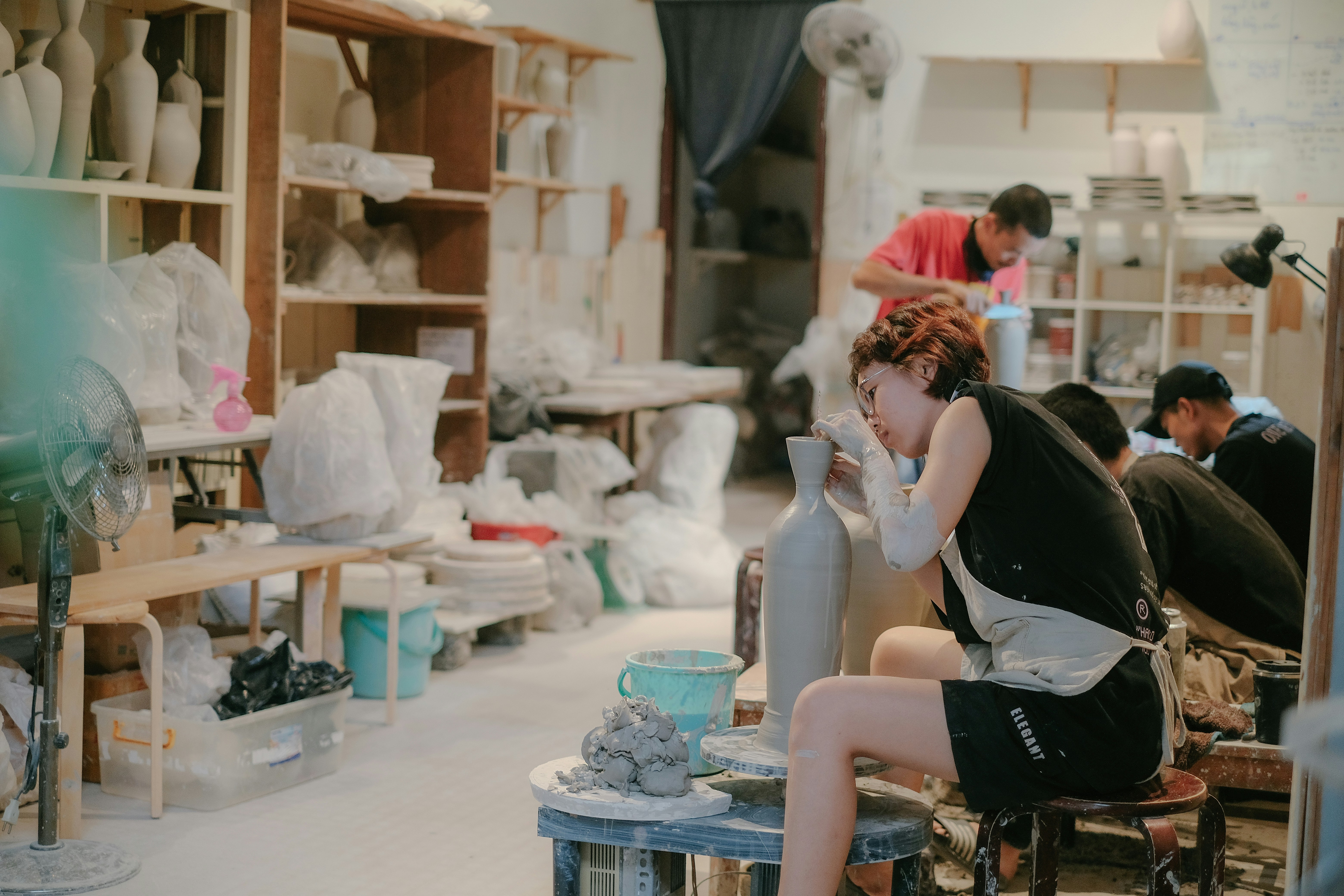 The shared studio with shelves of drying pots and a potter working at a table