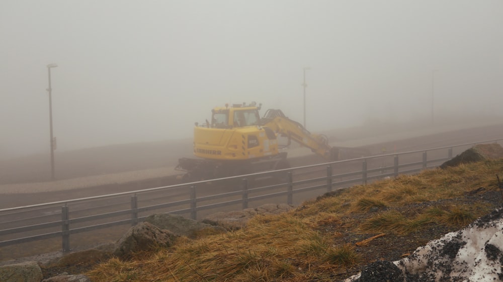 a yellow bulldozer driving down a road on a foggy day