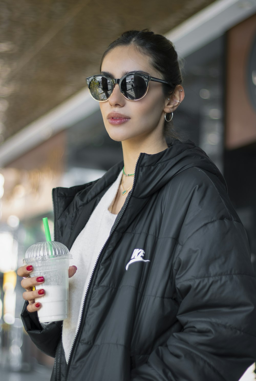 a woman in a black jacket and sunglasses holding a drink