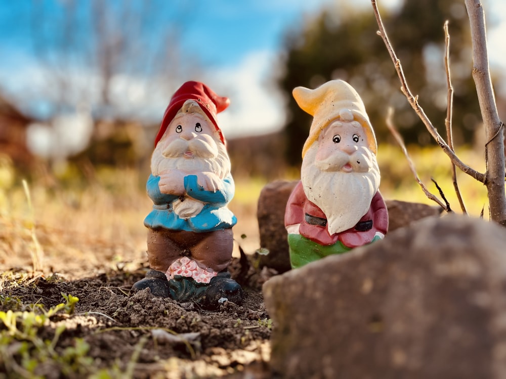 two garden gnomes sitting in the dirt next to a tree