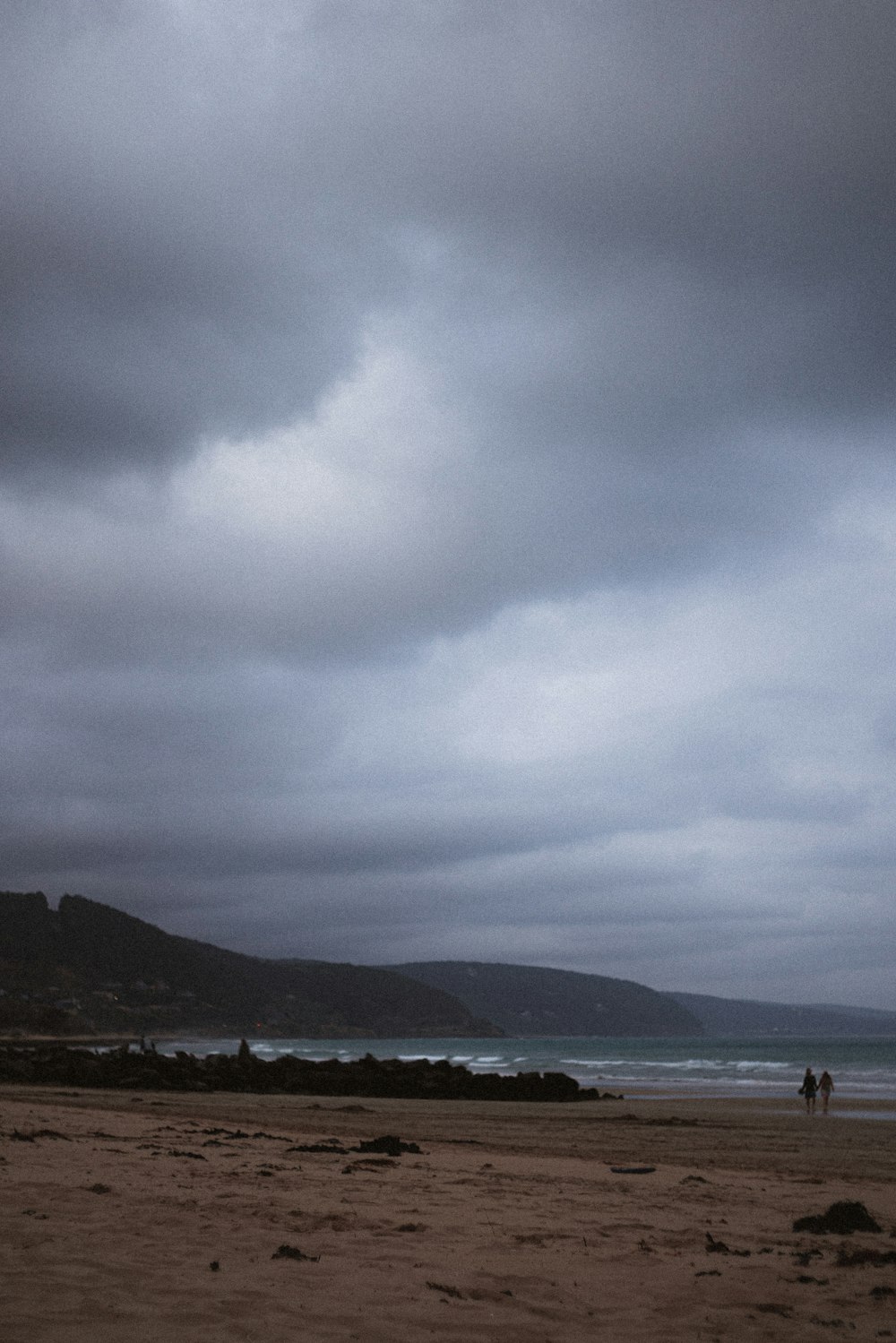 a couple of people walking on a beach under a cloudy sky