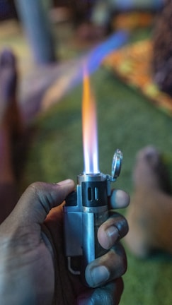 Close-up of a hand holding a sleek metal lighter with the charas smoke shop logo engraved.