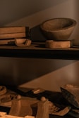 Several clay or ceramic molds of various shapes and sizes are arranged on dark shelves, casting shadows. The lighting creates an earthy and rustic ambiance.