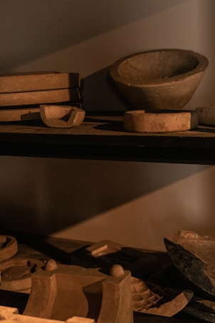 Several clay or ceramic molds of various shapes and sizes are arranged on dark shelves, casting shadows. The lighting creates an earthy and rustic ambiance.