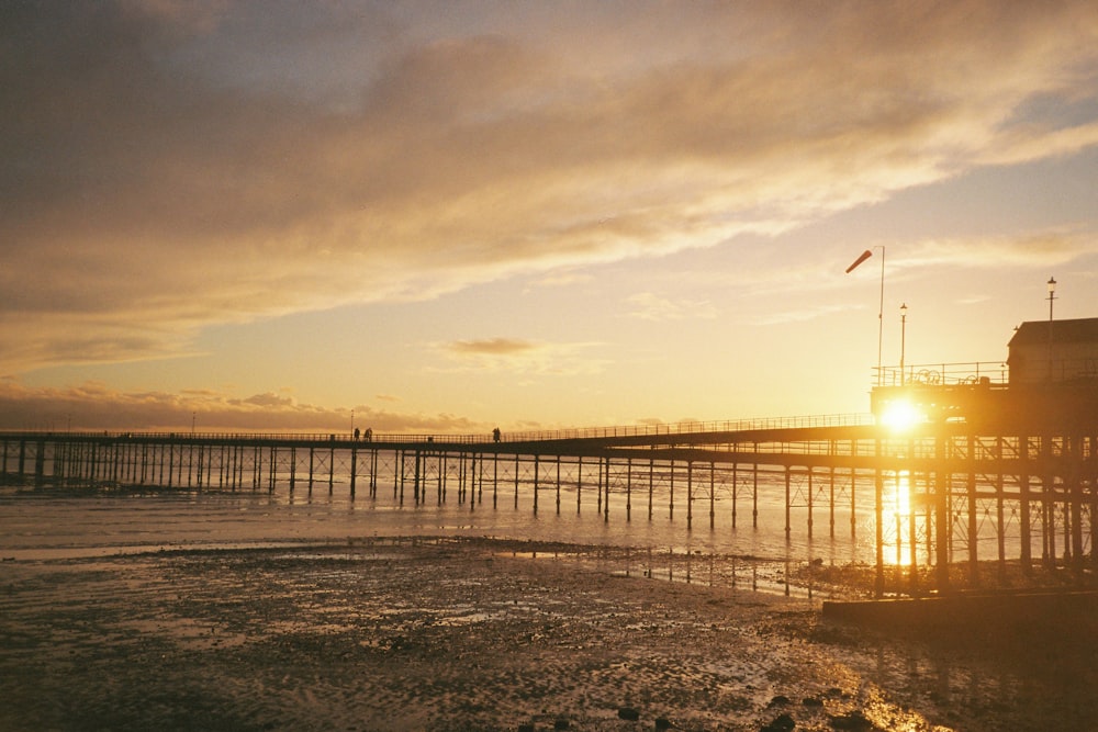 the sun is setting over the ocean and a pier