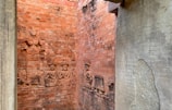 The image features ancient brick walls adorned with detailed bas-relief sculptures depicting figures in traditional attire. On the right, an engraved stone tablet includes several lines of intricate script, possibly an ancient language or inscription.