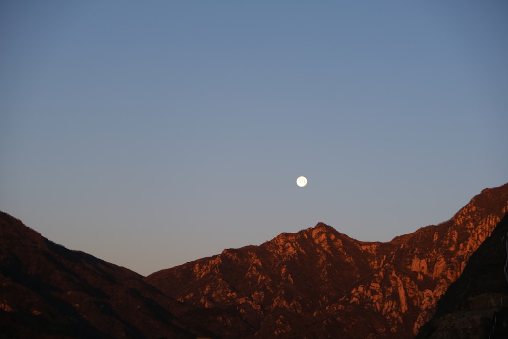 the moon is setting over a mountain range