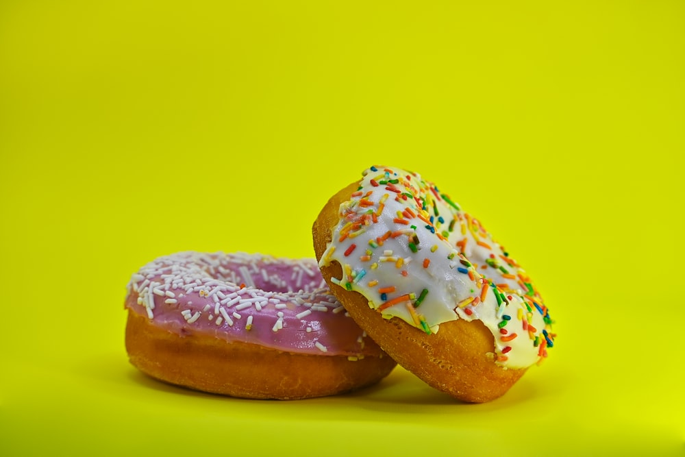 two donuts with sprinkles on a yellow background