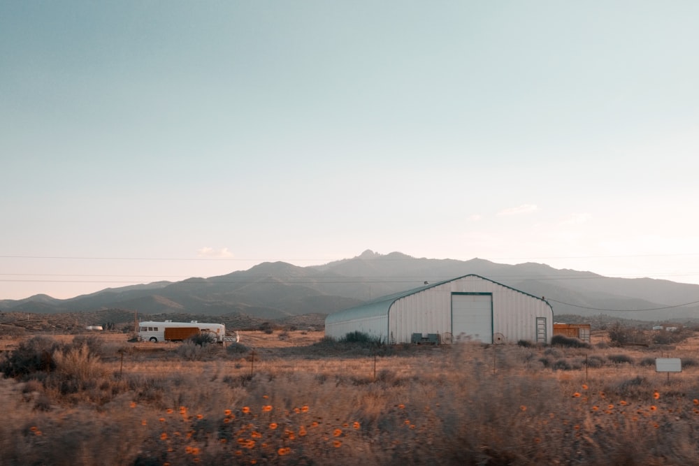 a barn in the middle of a field with mountains in the background